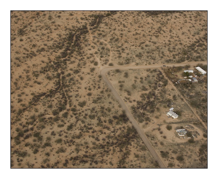  The bend in the road at the centre of this photograph is at Diamond Bells Ranch near Robles Junction. Diamond Bells was built as a restful and upscale desert retreat before the recent property market crash. In 2010, unbeknownst to the owner of the house volunteers from the American charity ‘The Samaritans” found the body of a Mexican migrant who had died very slowly of dehydration and exhaustion.&nbsp; 