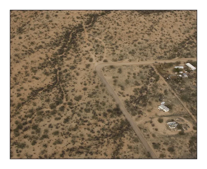  The bend in the road at the centre of this photograph is at Diamond Bells Ranch near Robles Junction. Diamond Bells was built as a restful and upscale desert retreat before the recent property market crash. In 2010, unbeknownst to the owner of the house volunteers from the American charity ‘The Samaritans” found the body of a Mexican migrant who had died very slowly of dehydration and exhaustion.&nbsp; 